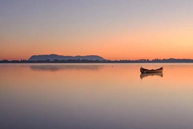 A lone canoe resting on still water at dawn