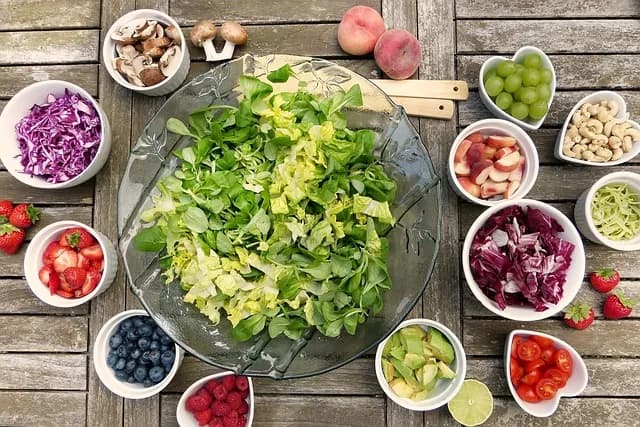 A large bowl of fresh salad surrounded by colourful vegetables and fruit
