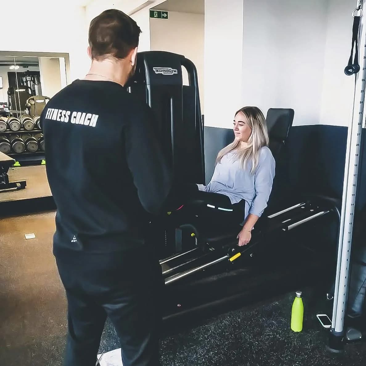 A fitness coach guiding a client through a leg press in the gym